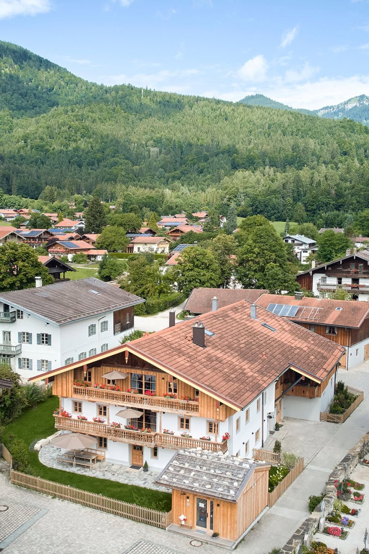 Der Oide Knoglerhof von oben. Im Vordergrund der kleine Hofladen und im Hintergrund die Berge und die grünen Bergwälder.